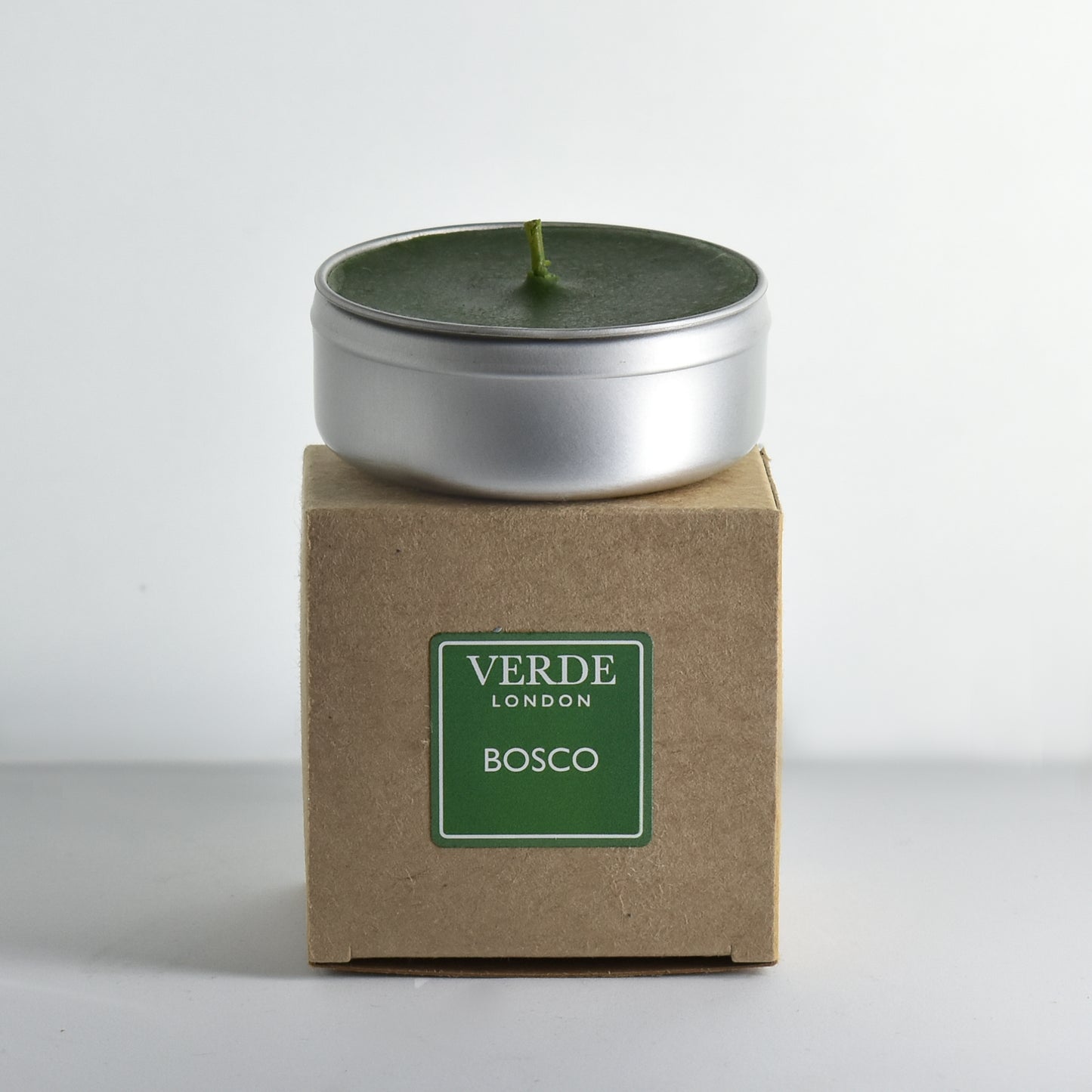 Candle in a metal tin on a cardboard box with a green label and 'Verde London' branding on a white background