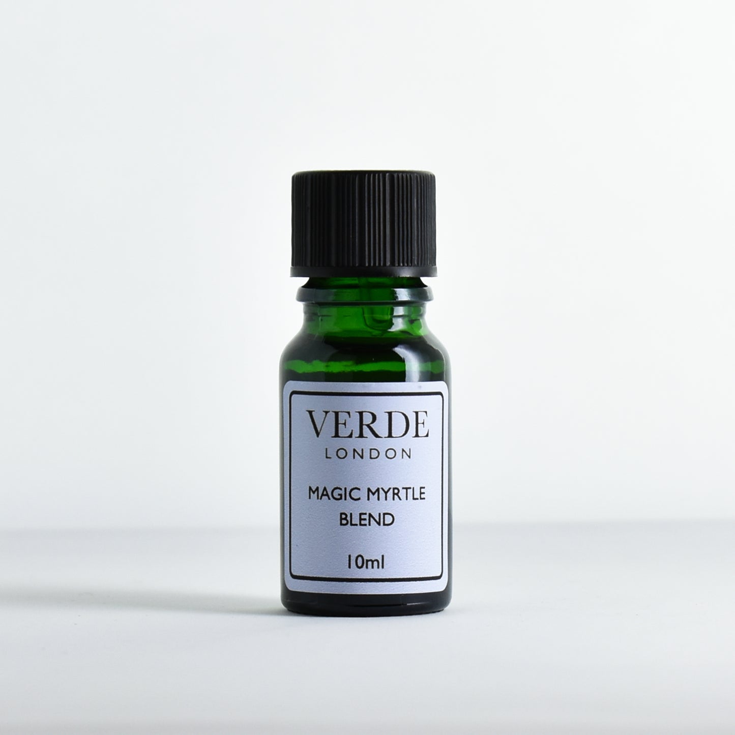 Green glass bottle of 'Magic Myrtle Blend' by Verde London with a pale blue label on a light gray background