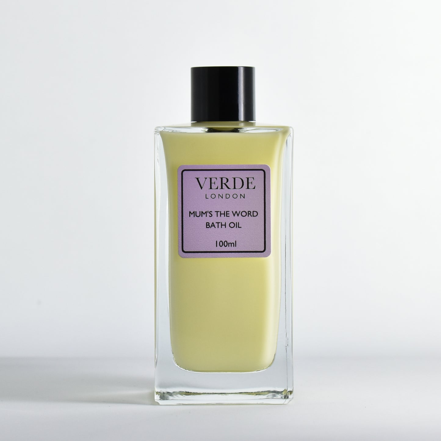 Bottle of Verde London 'mums the word' bath oil a yellowy millky colour with a pale purple label in a rectangular glass bottle on a white background
