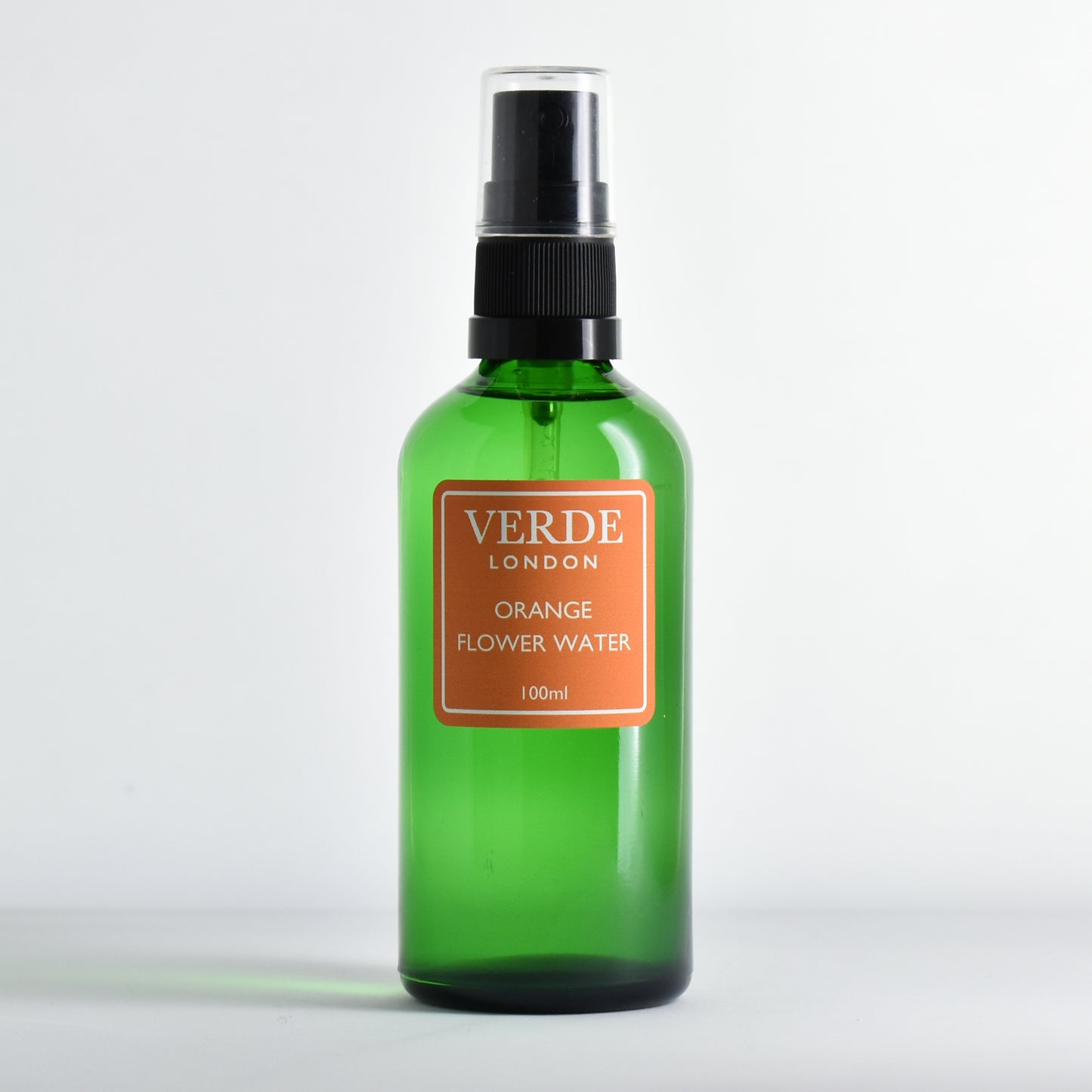 Green glass spray bottle of Orange Flower Water by the brand Verde London with an orange label on a white background
