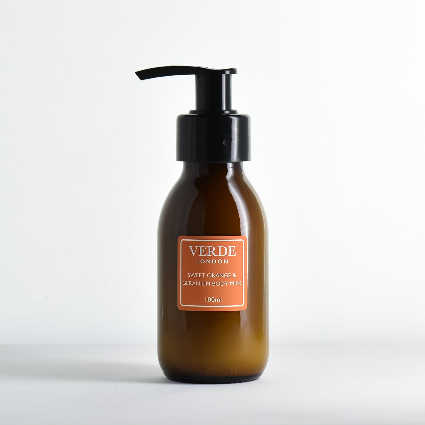 Amber bottle with pump of Sweet Orange and Geranium Body Milk with an orange label by the brand 'Verde London' on a white background