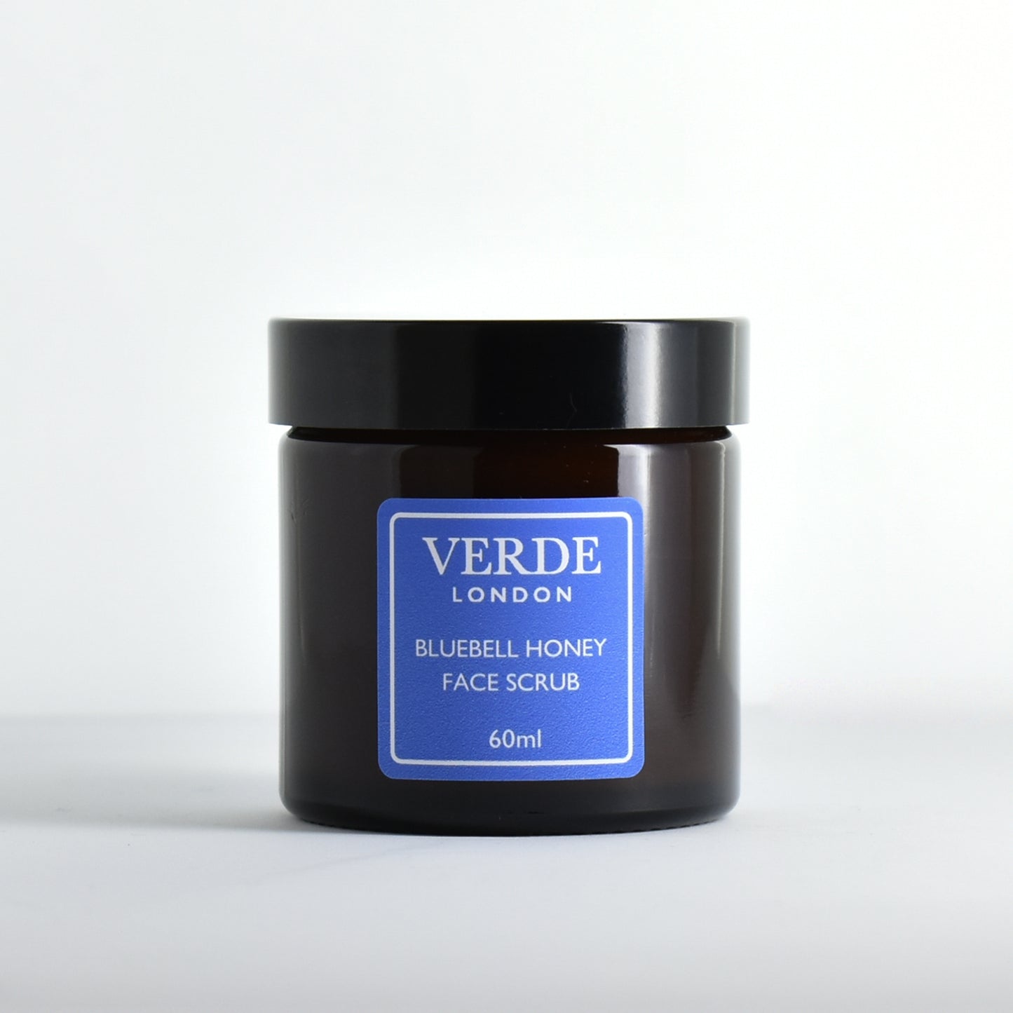 Amber glass jar of Verde London Bluebell Honey Face Scrub with a blue label on a white background
