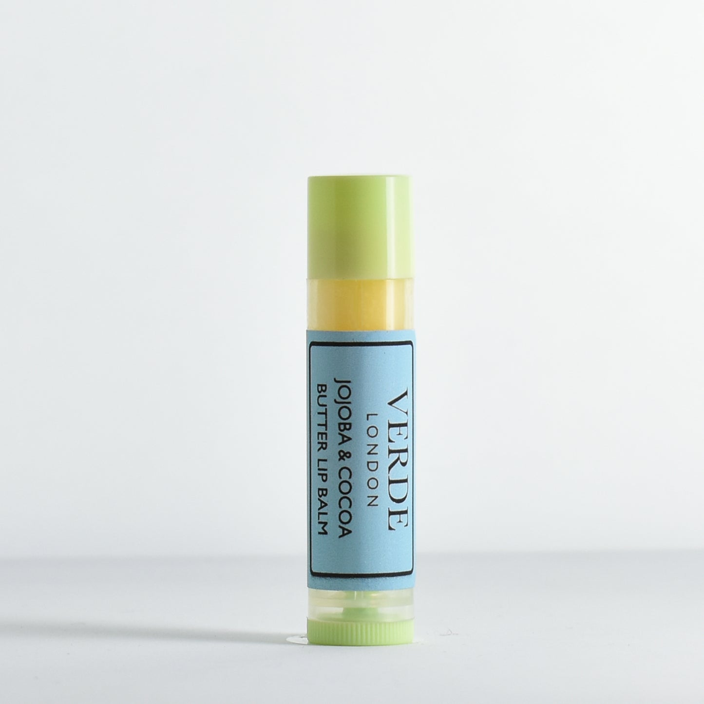 Jojoba and Cocoa Butter Lip balm with green cap and blue label by the brand Verde London on a white background