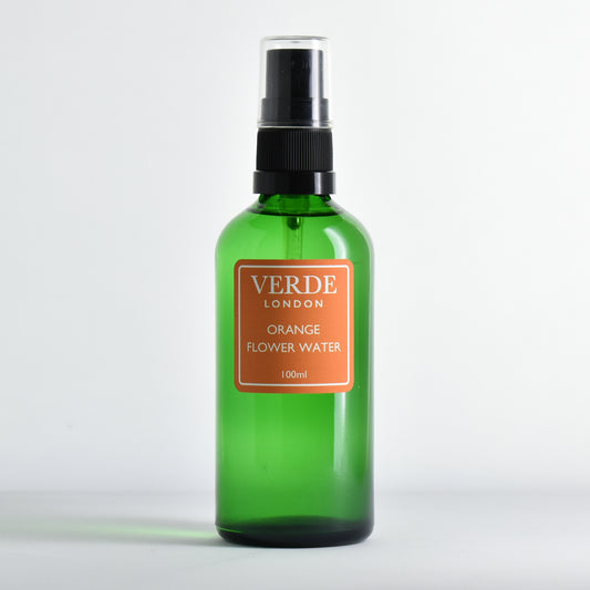 Green glass spray bottle of Orange Flower Water by the brand Verde London with an orange label on a white background