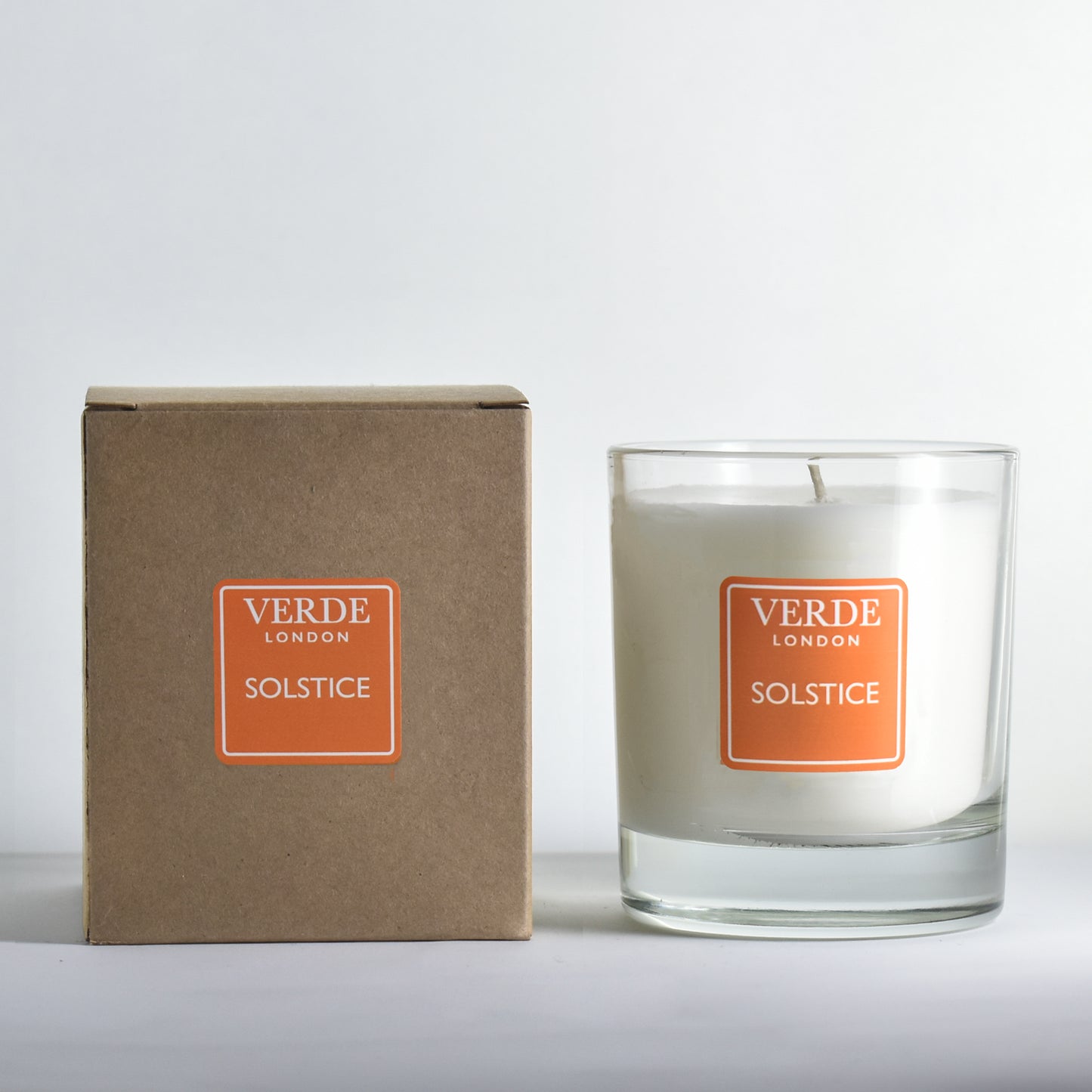 Candle and packaging with 'Verde London Solstice' orange label on a white background