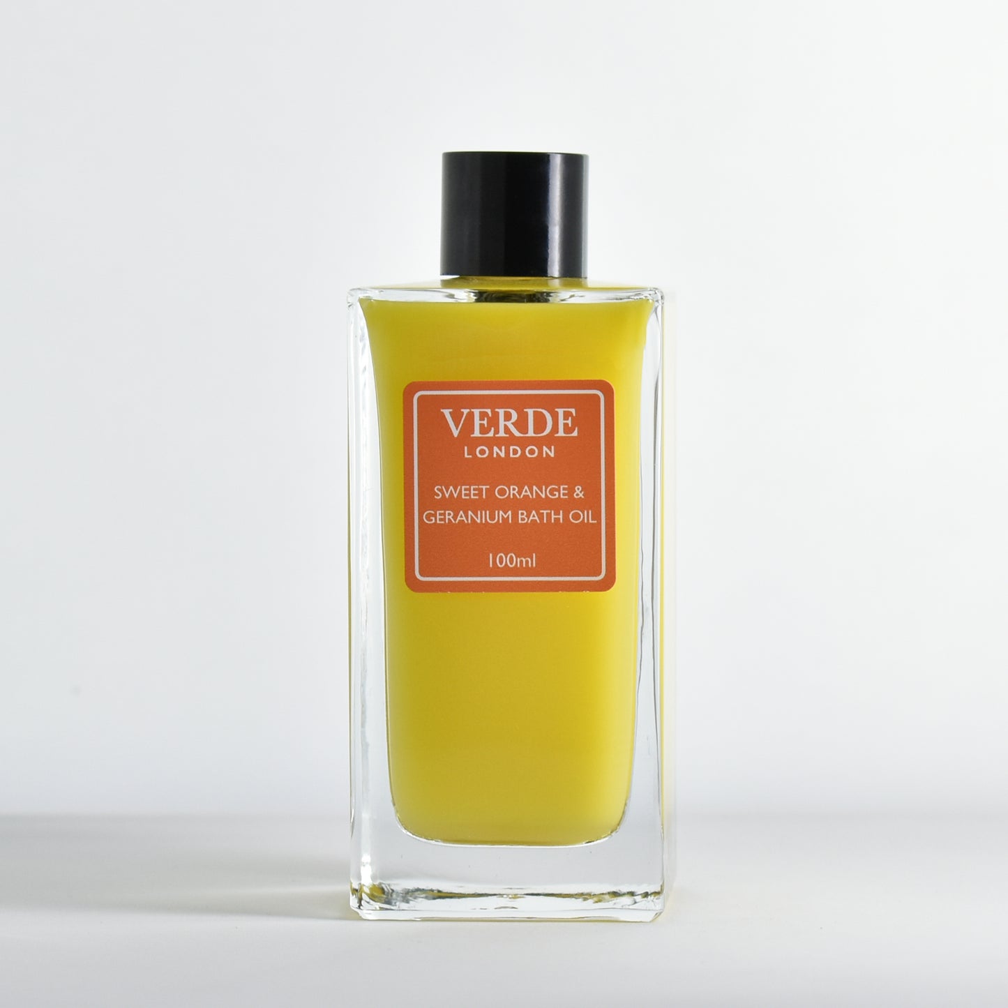 Bottle of Verde London Sweet Orange & Geranium Bath Oil 100ml, milky orange colour with an orange label in a rectangular glass bottle on a white background