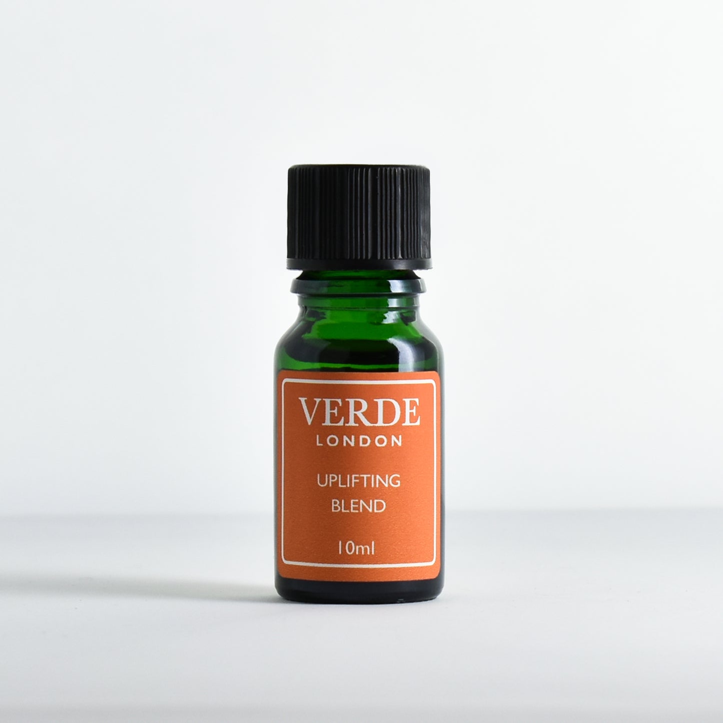 Green glass dropper bottle with orange  label containing 'Uplifting Blend' by Verde London on a white background.