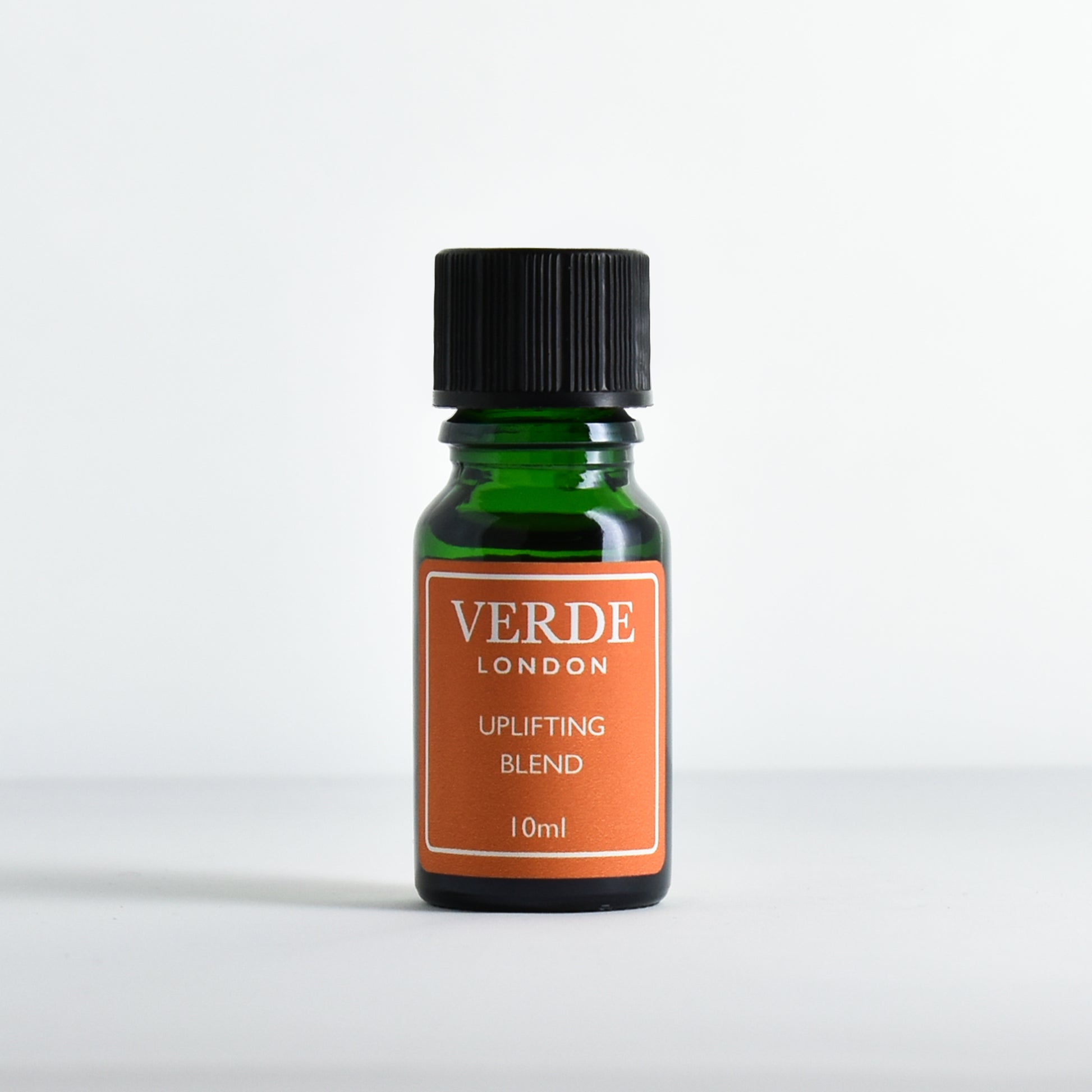 Green glass dropper bottle with orange  label containing 'Uplifting Blend' by Verde London on a white background.