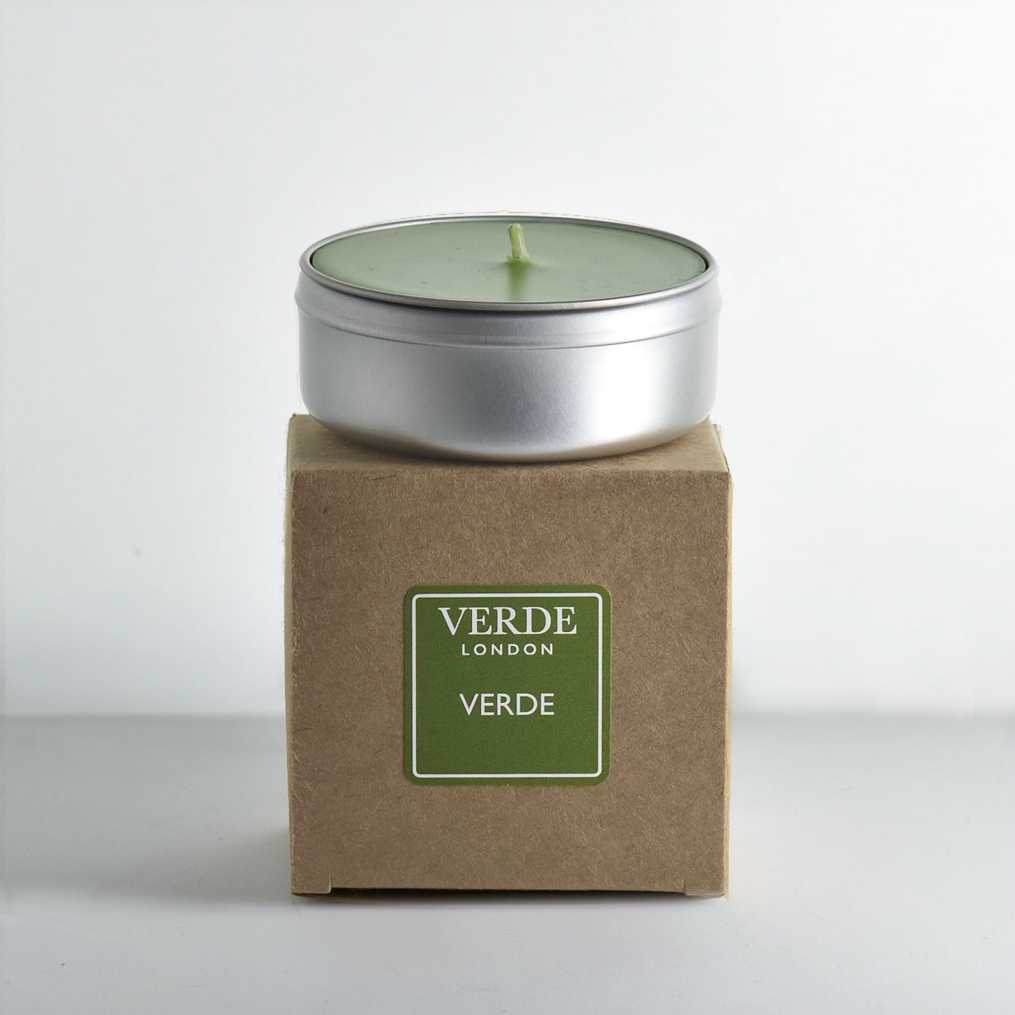 Candle in a metal tin on a cardboard box with 'Verde London' branding with a green label on a white background