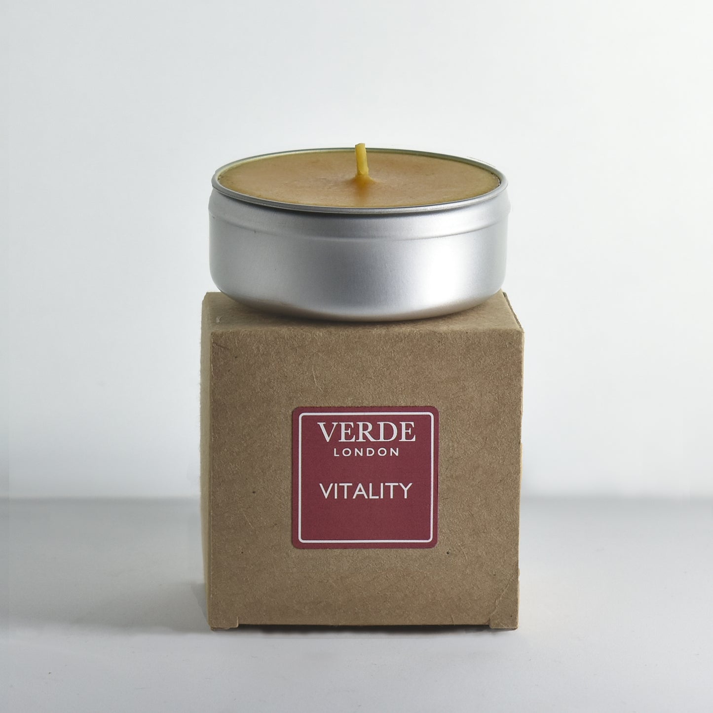 Candle in a metal tin on a cardboard box with a burgundy label and 'Verde London' branding on a white background